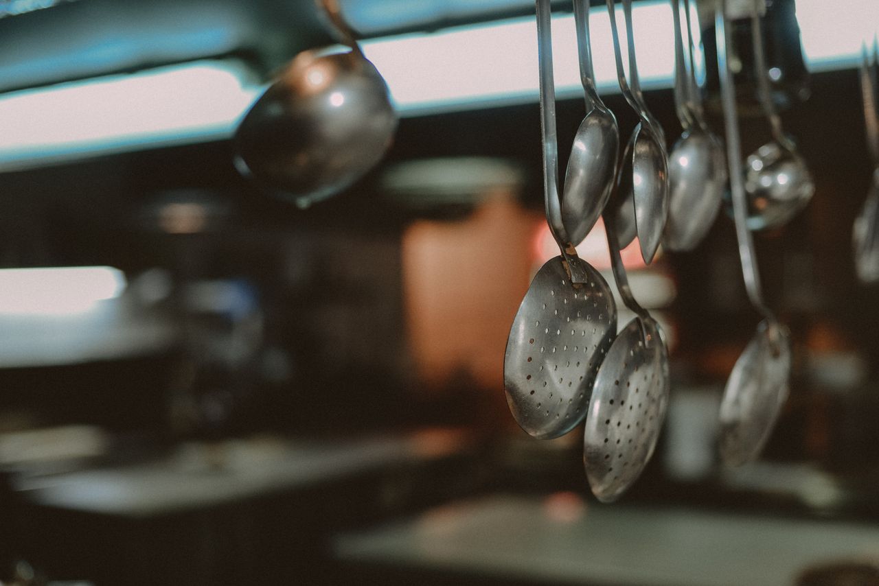 services-img Close-up of hanging metal spoons and ladles in a kitchen, blurred background