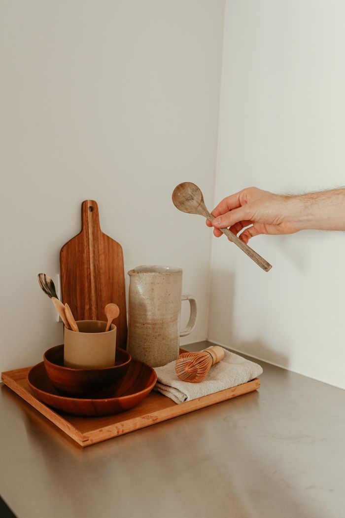 A minimalist kitchen setup with hand holding a wooden spoon, showcasing rustic tableware.